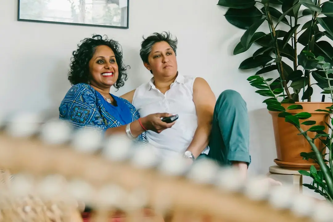 Two women relaxing on a sofa, one holding a TV remote, browsing the MyrixTV IPTV EPG